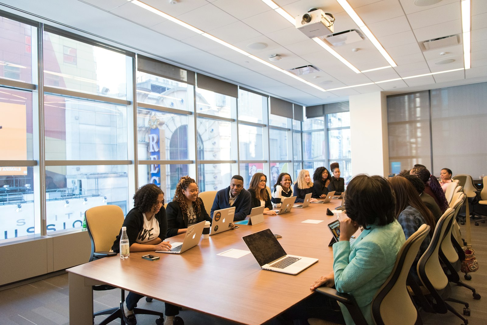 Diverse professional services team meeting around a conference table with laptops to discuss IT strategy in a bright office.