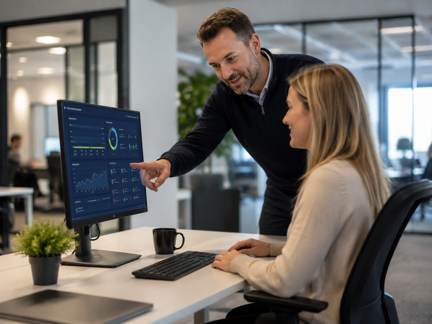 IT support technician helping an employee at her workstation while reviewing system monitoring dashboards, representing proactive managed IT support that prevents problems before they disrupt business operations.